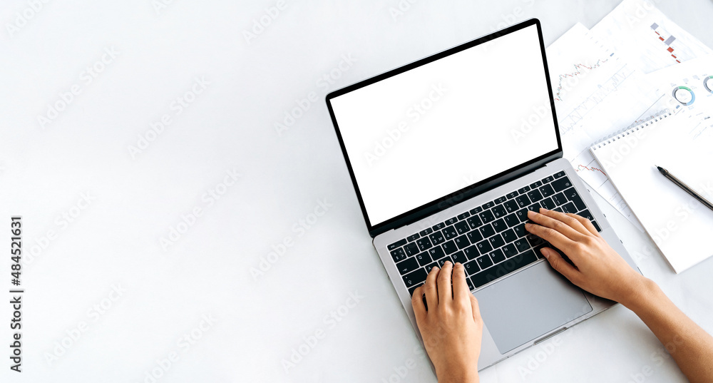 Copy space, mock-up concept. A laptop with a blank white screen, financial charts and a notepad lie nearby. Female hands on the keyboard, browsing the Internet, online correspondence Copy space, mock-up concept. A laptop with a blank white screen, financial charts and a notepad lie nearby. Female hands on the keyboard, browsing the Internet, online correspondence