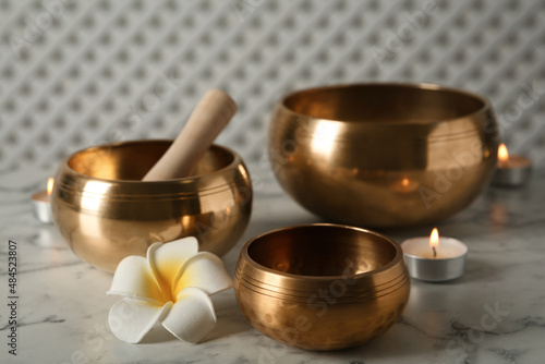 Tibetan singing bowls, mallet, plumeria flower and burning candles on white marble table