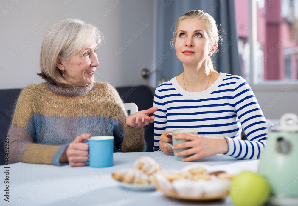 Two women drink tea and eat cakes. Mother with daughter