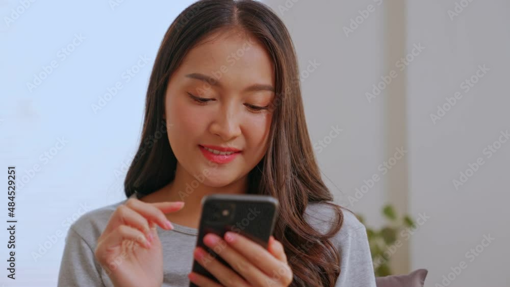 Happy Asian girl laughs with phone looking at mobile phone screen watching funny photo or video, enjoying pleasant distant communication in social network, web surfing or reading good news at home. Happy Asian girl laughs with phone looking at mobile phone screen watching funny photo or video, enjoying pleasant distant communication in social network, web surfing or reading good news at home.