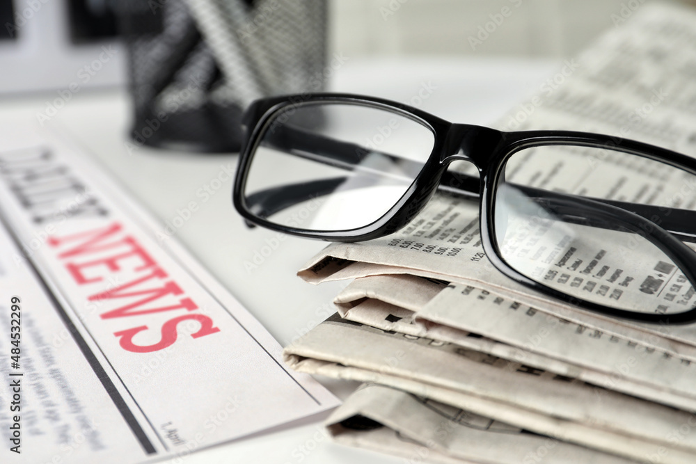 Stack of newspapers and glasses on white table, closeup Stack of newspapers and glasses on white table, closeup