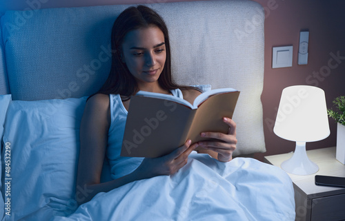 Young woman reading book in bed at night