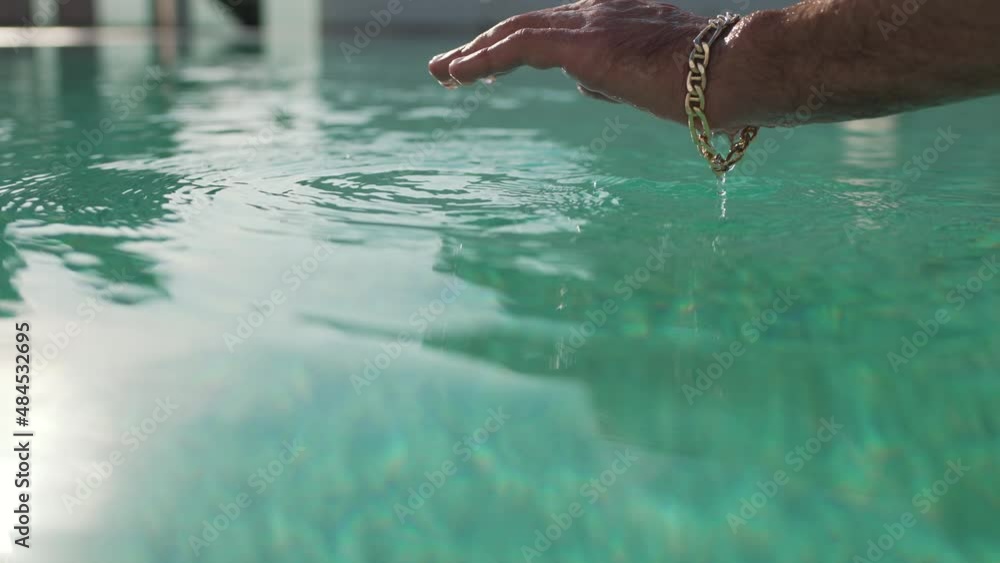 a man with a bracelet on his wrist dips his hand into the pool Stock