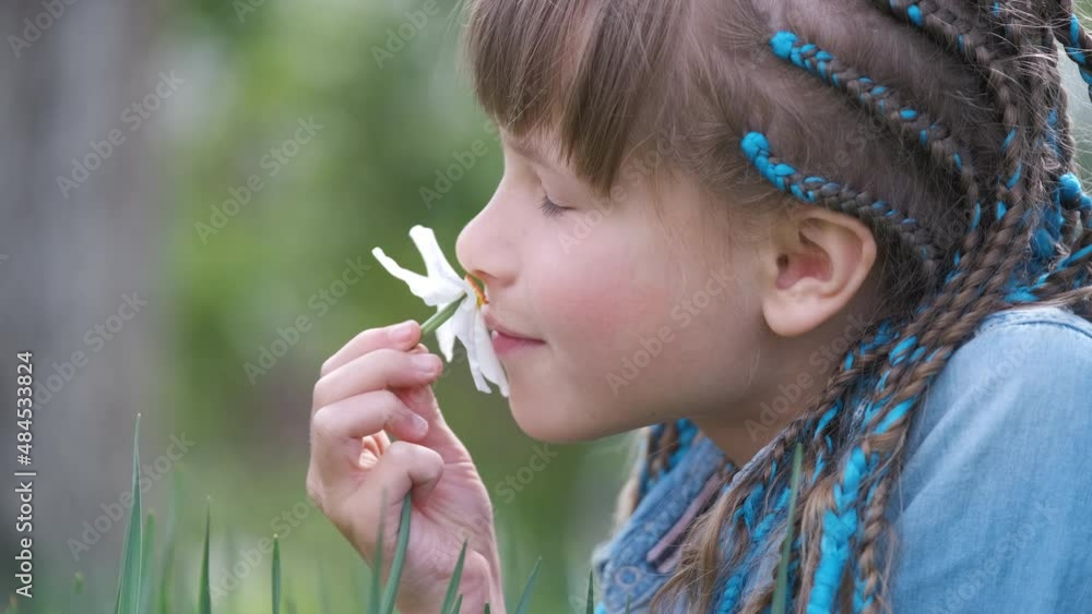 Happy child girl playing in summer garden enjoying sweet scent of white narcissus flowers on sunny day Happy child girl playing in summer garden enjoying sweet scent of white narcissus flowers on sunny day