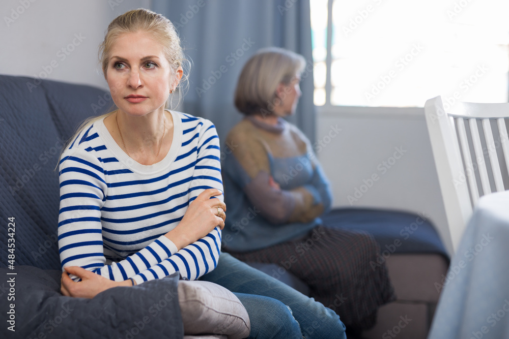 Adult daughter and her mature mother, sitting on opposite sides of the sofa in the same room, took offense at each other ..after a quarrel