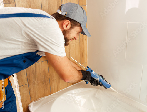Foto Concentrated plumber caulking bath tube with silicone glue using cartridge in ba