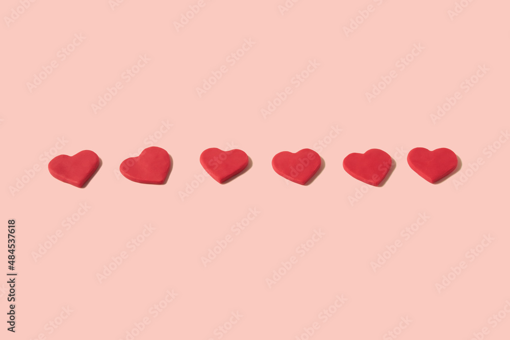 Lined up and centered red hearts made from modeling clay on a pastel pink background with copy space