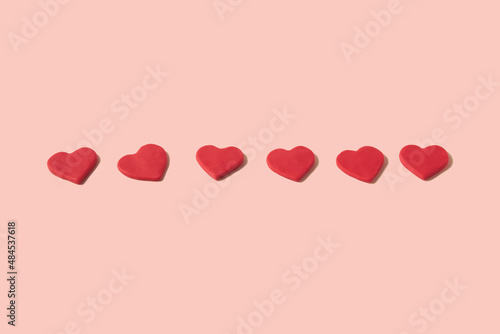 Lined up and centered red hearts made from modeling clay on a pastel pink background with copy space