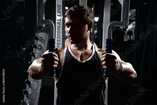 Muscular athletic young man fitness model do exercises in gym