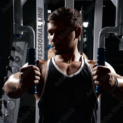 Muscular athletic young man fitness model do exercises in gym