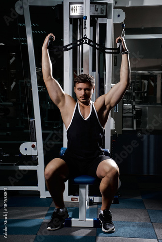 Muscular athletic young man fitness model do exercises in gym