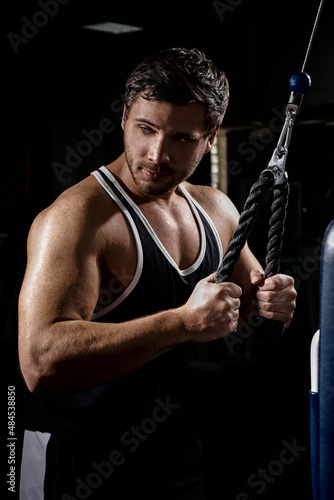 Muscular athletic young man fitness model do exercises in gym