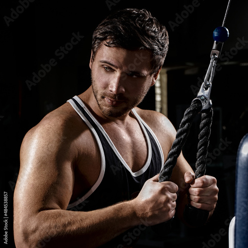 Muscular athletic young man fitness model do exercises in gym