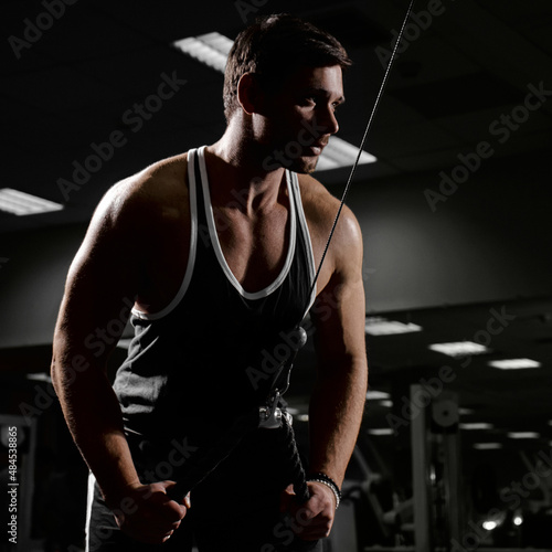 Muscular athletic young man fitness model do exercises in gym