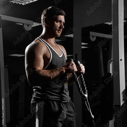 Muscular athletic young man fitness model do exercises in gym