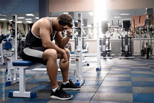 Muscular athletic young man fitness model sitting tired after exercises in gym black and white