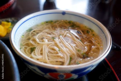 On a white porcelain plate, clear soup and noodles.