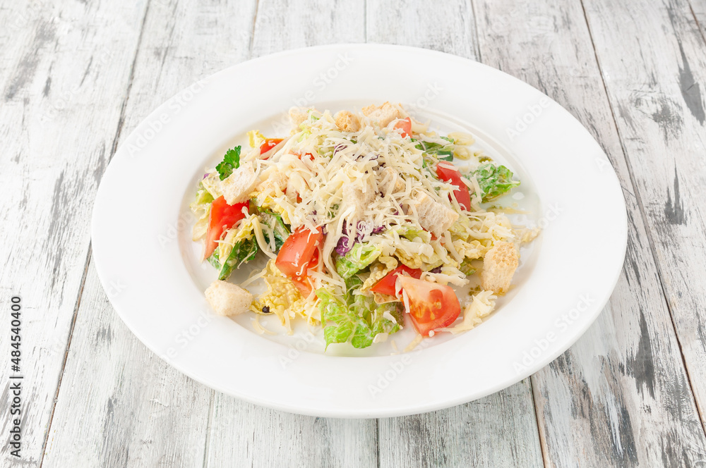 Caesar salad with chicken. In a white plate. Light wooden background. View from above. Caesar salad with chicken. In a white plate. Light wooden background. View from above.