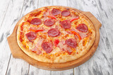 Pizza with pork breast, salami sausage, sweet paprika and mozzarella cheese. On a round wooden board. Light wooden background. View from above.