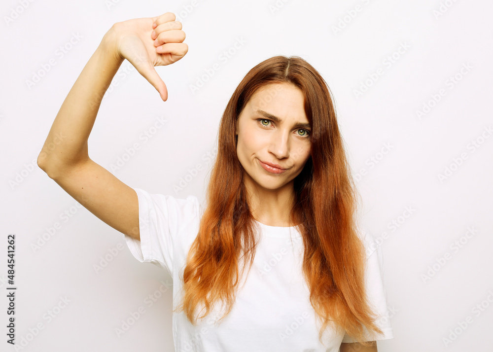 redhair woman shows diapproval sign, keeps thumb down, expresses dislike redhair woman shows diapproval sign, keeps thumb down, expresses dislike