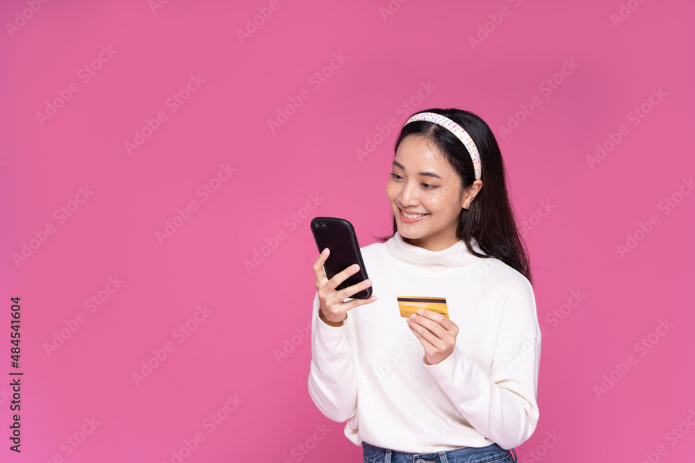 Beautiful Asia women smile use smartphone and credit card purchase online shopping and excited with success payment on isolated pink background Beautiful Asia women smile use smartphone and credit card purchase online shopping and excited with success payment on isolated pink background