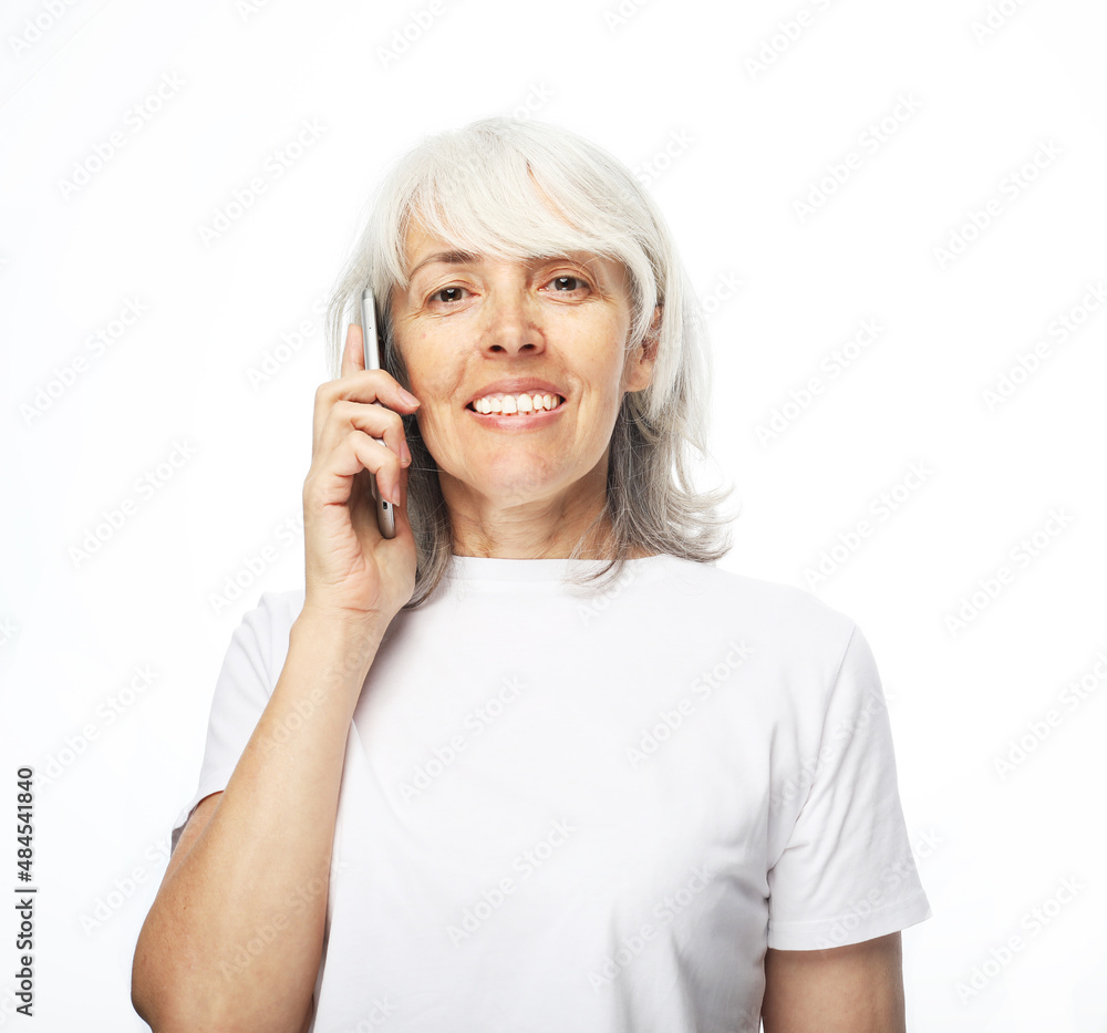 Portrait of attractive senior woman wearing white t-shirt talking by mobile phone. Studio shot. Portrait of attractive senior woman wearing white t-shirt talking by mobile phone. Studio shot.