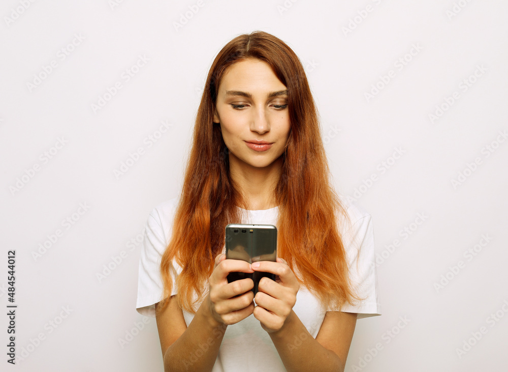 Smiling lovely young woman standing and using cell phone over grey background Smiling lovely young woman standing and using cell phone over grey background
