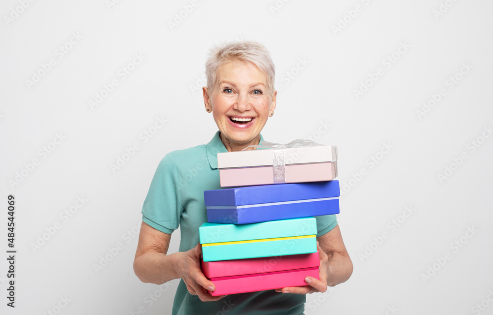 Elderly woman 60s holding present boxes with gifts isolated on white grey background Elderly woman 60s holding present boxes with gifts isolated on white grey background