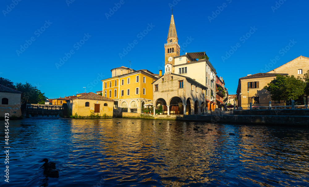Catholic oratory of Madonna della Pesqueria and belfry of St. Andrew Cathedral on bank on Lemene river in Portogruaro, Veneto, Italy..