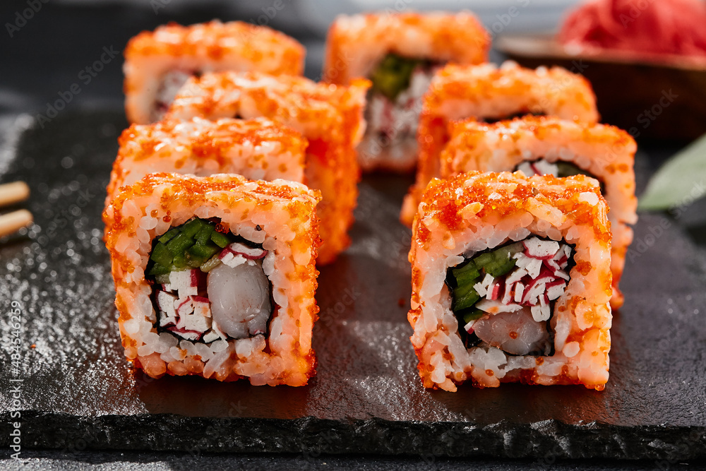Maki sushi on dark stone table. California maki with tobiko. Sushi