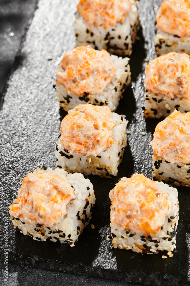 Baked Maki sushi on dark slate. Hot sushi roll with salmon and cheese. Sushi roll sesame outside, baked salmon and cheese topped. Style concept japanese menu with black background Baked Maki sushi on dark slate. Hot sushi roll with salmon and cheese. Sushi roll sesame outside, baked salmon and cheese topped. Style concept japanese menu with black background