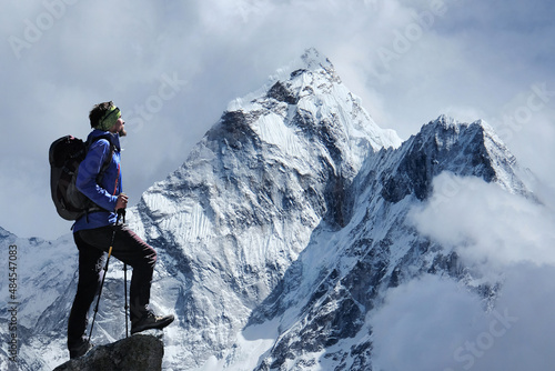 Hiker with backpack standing on high cliff and enjoying the Ama Dablam mountain view on Everest Base Camp trek in Himalayas. Success, freedom, active sport concept