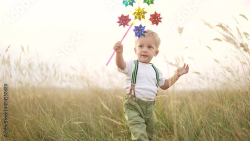 kid walk pinwheel. little baby boy play with windmill toy wind in the park. happy family kid dream concept. baby boy play toy pinwheel walk sun the glare of sunset at fun in the park photo