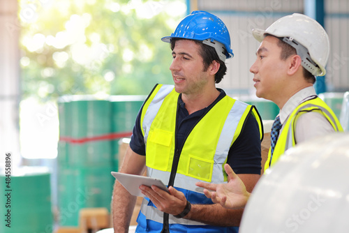 Architect or engineering men and worker standing and checking large warehouse with tablet. Multiethnic two business manager controlling work at warehouse industry building.