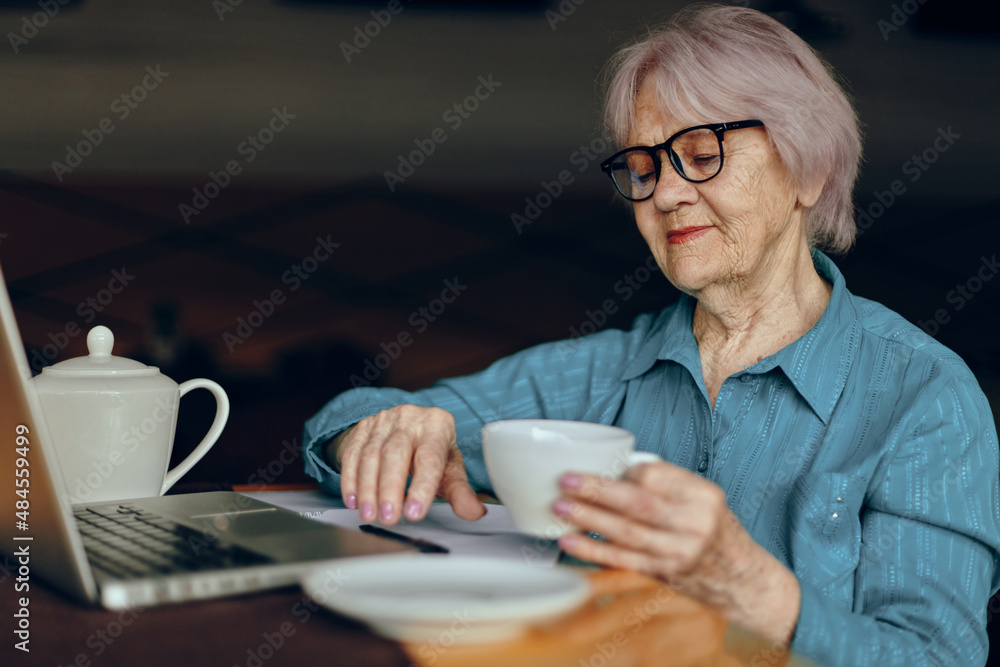 elderly woman with glasses sits at a table in front of a laptop unaltered elderly woman with glasses sits at a table in front of a laptop unaltered