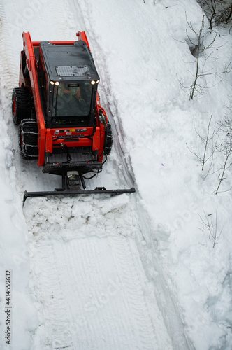 small tractor with chains on wheels pushing snow with blade snow ploughing to clear walkway clearing snow from path in winter after heavy snowfall viewed from above vertical format room for type 
