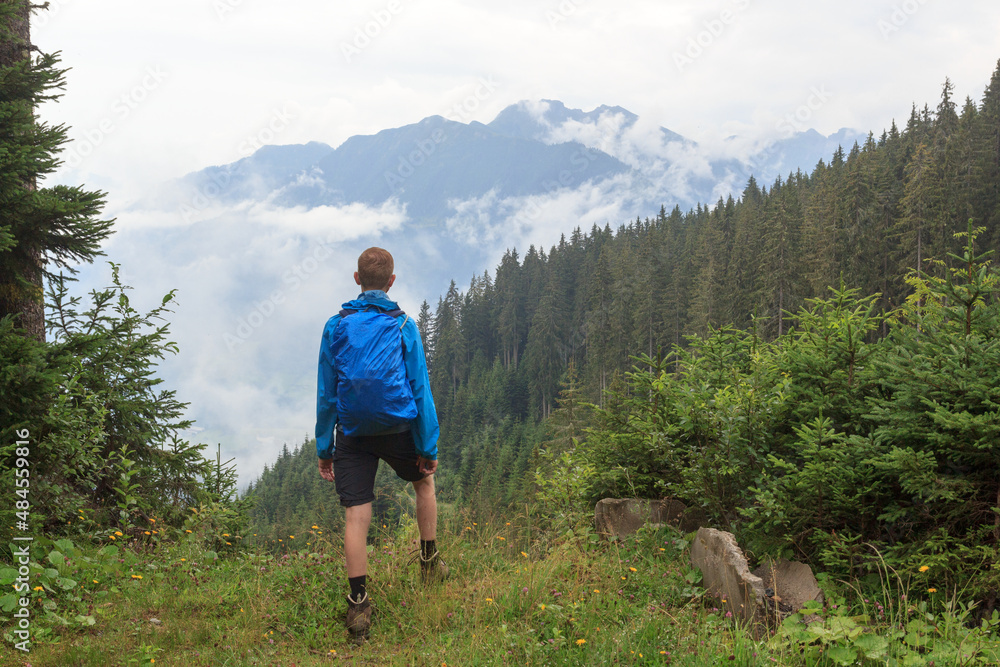 Panorama view with male hiker man in rainwear standing in front of alpine mountains and clouds in Salzburgerland, Austria