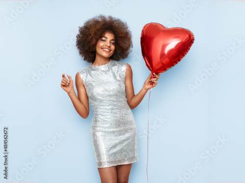 A beautiful young African-American woman with heart shape air balloon on a blue background. Woman on Valentine's Day. Symbol of love photo