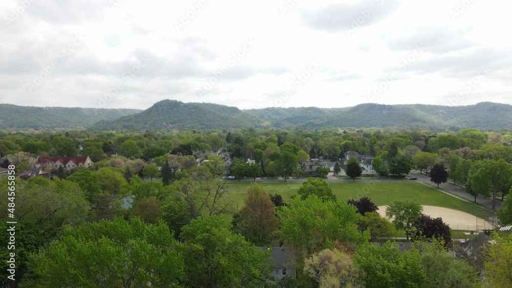 Residential neighborhood of older homes surrounding a well maintained city park on a gray cloudy day. Rolling hills covered in trees in the background. Residential neighborhood of older homes surrounding a well maintained city park on a gray cloudy day. Rolling hills covered in trees in the background.
