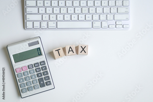 The word Tax on top of wooden cubes next to calculator and keyboard. Tax filing concept.