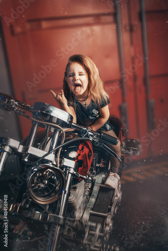 Stylish baby brunette in a leather dress showing her tongue against the background of the garage. bikers free ride