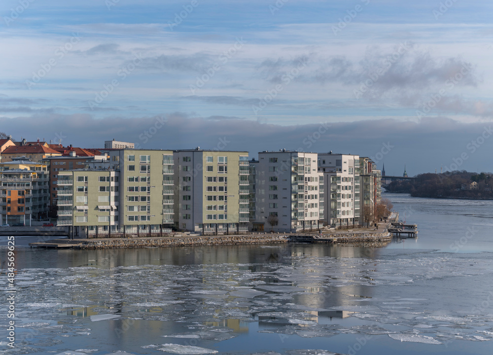 Apartment houses at the waterfront of the district island Lilla Essingen, ice floats and reflections a cold sunny winter day in Stockholm