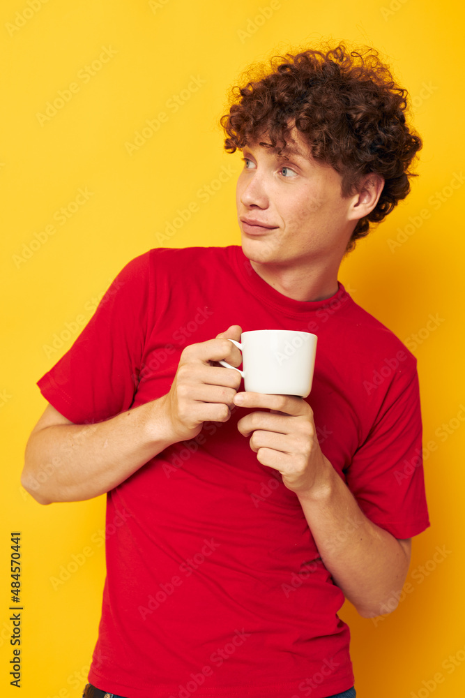 Young curly-haired man posing with a white mug and in the hands of a drink yellow background unaltered Young curly-haired man posing with a white mug and in the hands of a drink yellow background unaltered