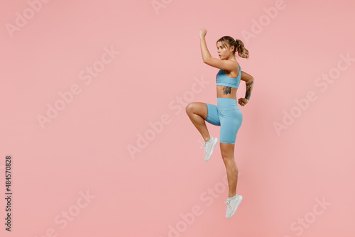 Full body young strong sporty athletic fitness trainer instructor woman 20s wear blue tracksuit spend time in home gym jump high run isolated on pastel plain pink background. Workout sport concept