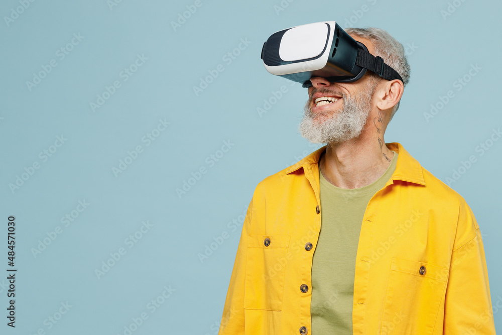 Elderly fun amazed happy gray-haired mustache bearded man 50s in yellow  shirt watching in vr headset pc gadget isolated on plain pastel light blue  background studio portrait. People lifestyle concept. foto de