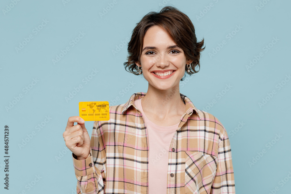 Young smiling rich satisfied happy woman 20s wearing casual brown shirt hold in hand credit bank card isolated on pastel plain light blue color background studio portrait. People lifestyle concept Young smiling rich satisfied happy woman 20s wearing casual brown shirt hold in hand credit bank card isolated on pastel plain light blue color background studio portrait. People lifestyle concept