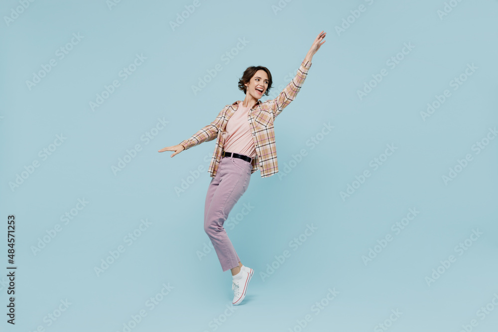 Full body young smiling happy woman 20s wearing casual brown shirt stand on toes dance leaning back fooling around isolated on pastel plain light blue color background studio People lifestyle concept