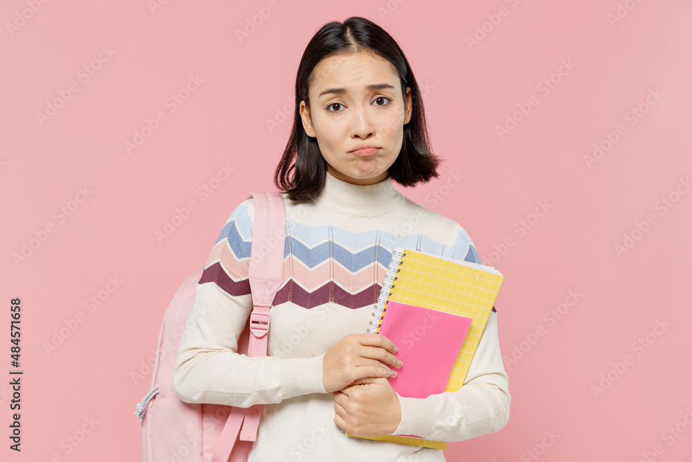 Sad serious displeased teen student girl of Asian ethnicity wear sweater backpack hold books look camera isolated on pastel plain light pink color background Education in university college concept. Sad serious displeased teen student girl of Asian ethnicity wear sweater backpack hold books look camera isolated on pastel plain light pink color background Education in university college concept.