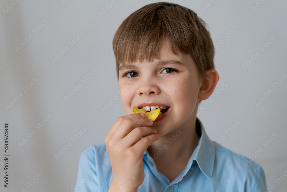 Close up portrait cheerful child having fun eating potato chips isolated on gray background. Cute little boy eating chips and smiling looking at the camera. Caucasian child eats junk food Close up portrait cheerful child having fun eating potato chips isolated on gray background. Cute little boy eating chips and smiling looking at the camera. Caucasian child eats junk food