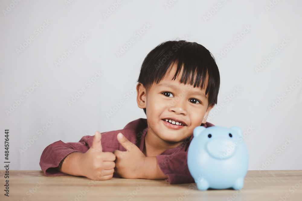 Saving concept, boy sitting on table with piggy bank, learning to save money Saving concept, boy sitting on table with piggy bank, learning to save money